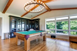 Una mesa de billar en una habitación con pisos de madera y un ventanal grande.