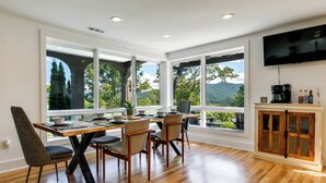 A dining area with a wooden table and chairs, large windows with a view of trees and mountains, and a kitchen area with a coffee machine and cabinets. - 32-acre Escape w/ Trails & Games! Gateway to Gsmnp (Franklin)