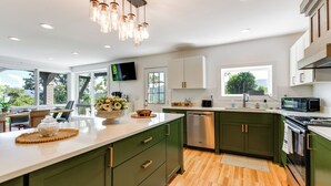 A modern kitchen with a large island, green cabinets, and a flat-screen TV. - 32-acre Escape w/ Trails & Games! Gateway to Gsmnp (Franklin)