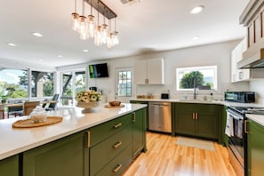 A modern kitchen with a large island, green cabinets, and a flat-screen TV. - 32-acre Escape w/ Trails & Games! Gateway to Gsmnp (Franklin)