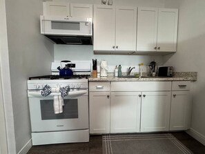 Uma cozinha com armários brancos, fogão e micro-ondas.
