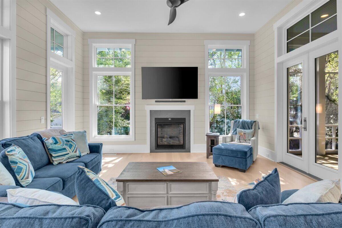 A spacious living room with a fireplace, a flat-screen TV, and large windows.