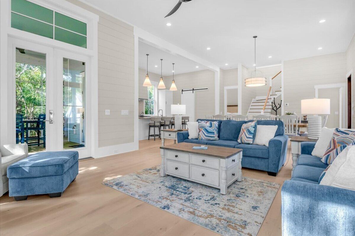 Step into your bright, open living space with soaring ceilings, stylish coastal furnishings, and natural light pouring through glass doors—perfect for relaxing or gathering together.
