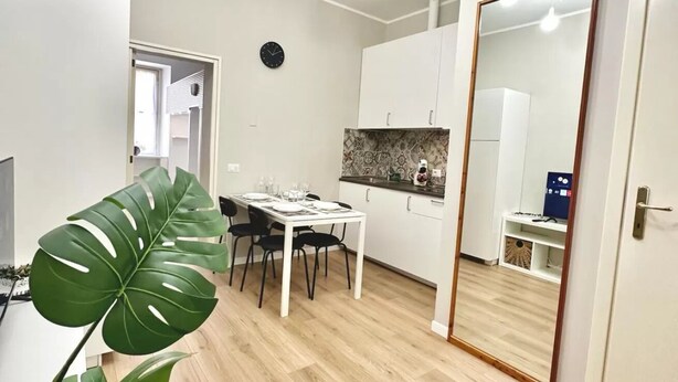 Ett kompakt kök med vita skåp, ett matbord med plats för fyra personer och en stor spegel.