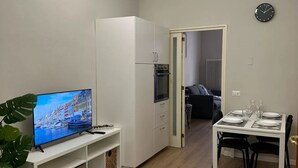 Ett kompakt bostadsutrymme med ett litet kök, en matplats och en tv som visar en vacker utsikt över staden.