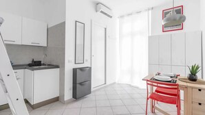 A modern kitchen with white cabinets, a grey refrigerator, a dining area with a red chair, and a small table.