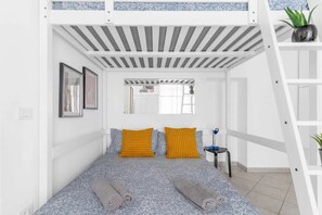 Een slaapkamer met een stapelbed, een plafond in wit en grijs gestreept, een tafeltje met een plantje en een spiegel aan de muur.