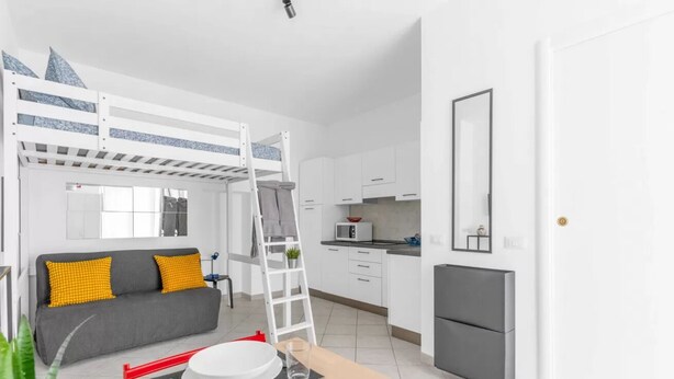 A modern apartment with a bunk bed, kitchenette, dining area, and a sofa with cushions.