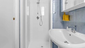 Uma casa de banho moderna com cabine de duche em vidro, lavatório branco e dispensador de sabonete amarelo numa parede com azulejos azuis.