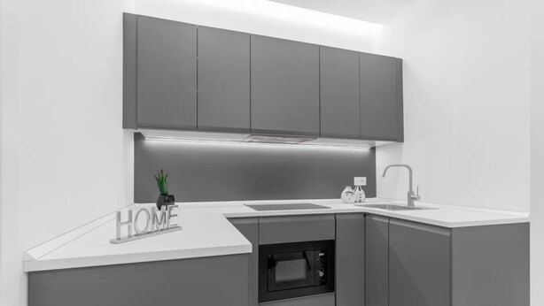 Une cuisine moderne avec des meubles de couleur grise, un four encastré et un plan de travail doté d’un évier et d’un robinet.