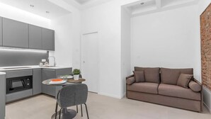 Une cuisine moderne avec des meubles gris, un coin repas avec une chaise grise et un canapé marron.