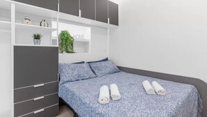 Une chambre à coucher avec un lit, une armoire et une étagère sur laquelle se trouvent une plante et une horloge.