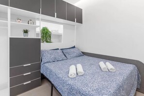 A bedroom with a bed, a wardrobe, and a shelf with a plant and a clock.