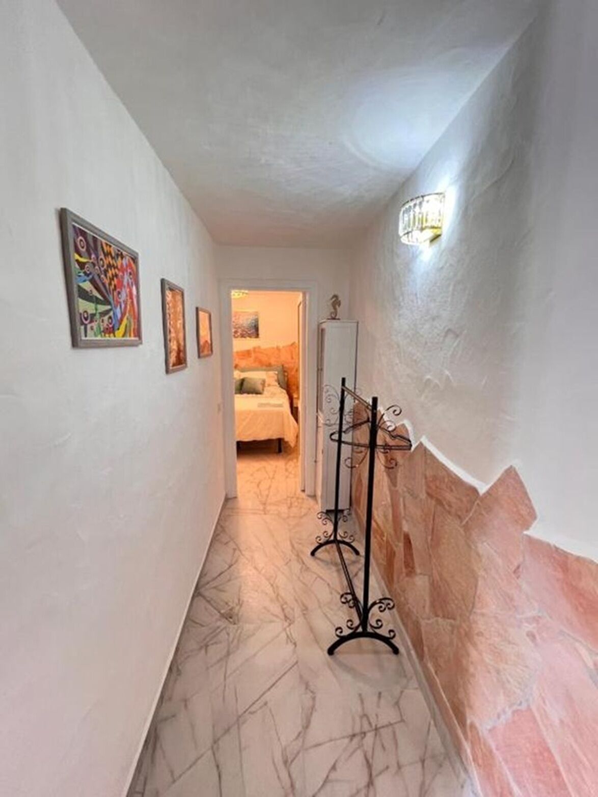 A hallway with marble flooring, a coat rack, and artwork on the walls.