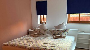 Quarto com cama, mesas de cabeceira e janela com persianas.