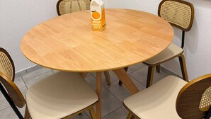 Uma mesa de madeira redonda com quatro cadeiras, um pacote de suco de laranja e um espelho na parede.