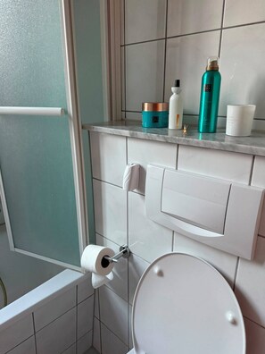 A bathroom with a toilet, a paper towel holder, and a shelf with toiletries. - Vacation Rental in the Heart of Erfurt (Erfurt)