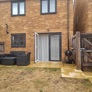 A brick building with a sliding glass door, a patio with wicker furniture, and a barbecue grill. - New 3 bedroom home with2 Front door parking (East Tilbury)