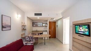 A compact living space with a red sofa, a dining table, a kitchen area, and a TV mounted on the wall. - SHB Beachfront Varanda e Piscina (Santos)