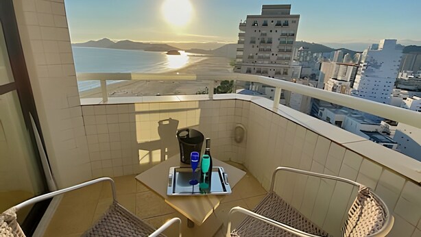 Un balcón con una mesa, dos sillas y vista a la playa y al paisaje urbano.