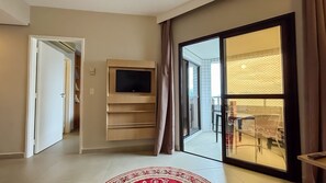 A modern living room with a flat-screen TV, a sliding glass door to a balcony, and a patterned rug. - SHB Beachfront Varanda e Piscina (Santos)