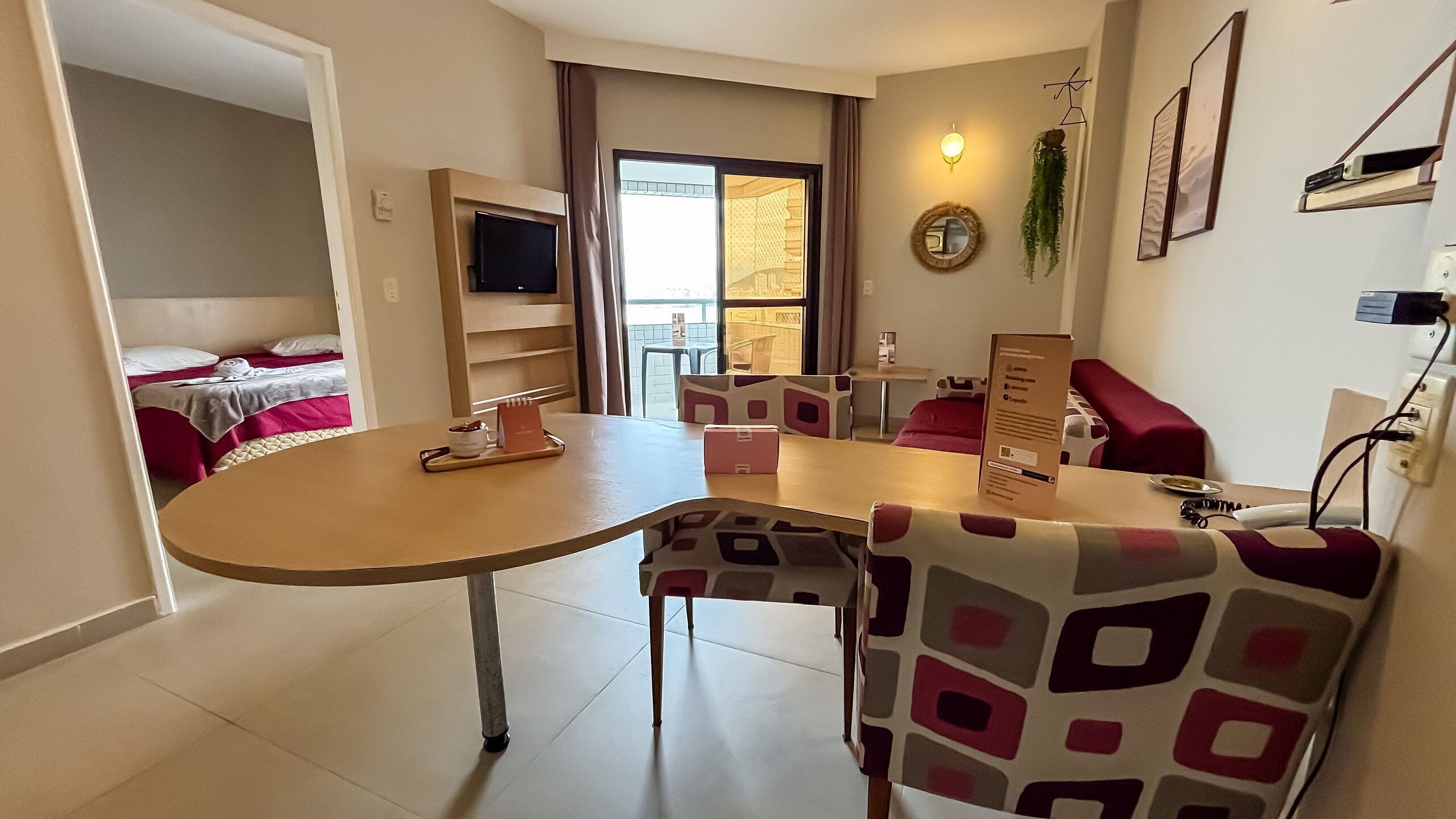 A hotel room with a dining area, a bed, a TV, and a view of the outside.