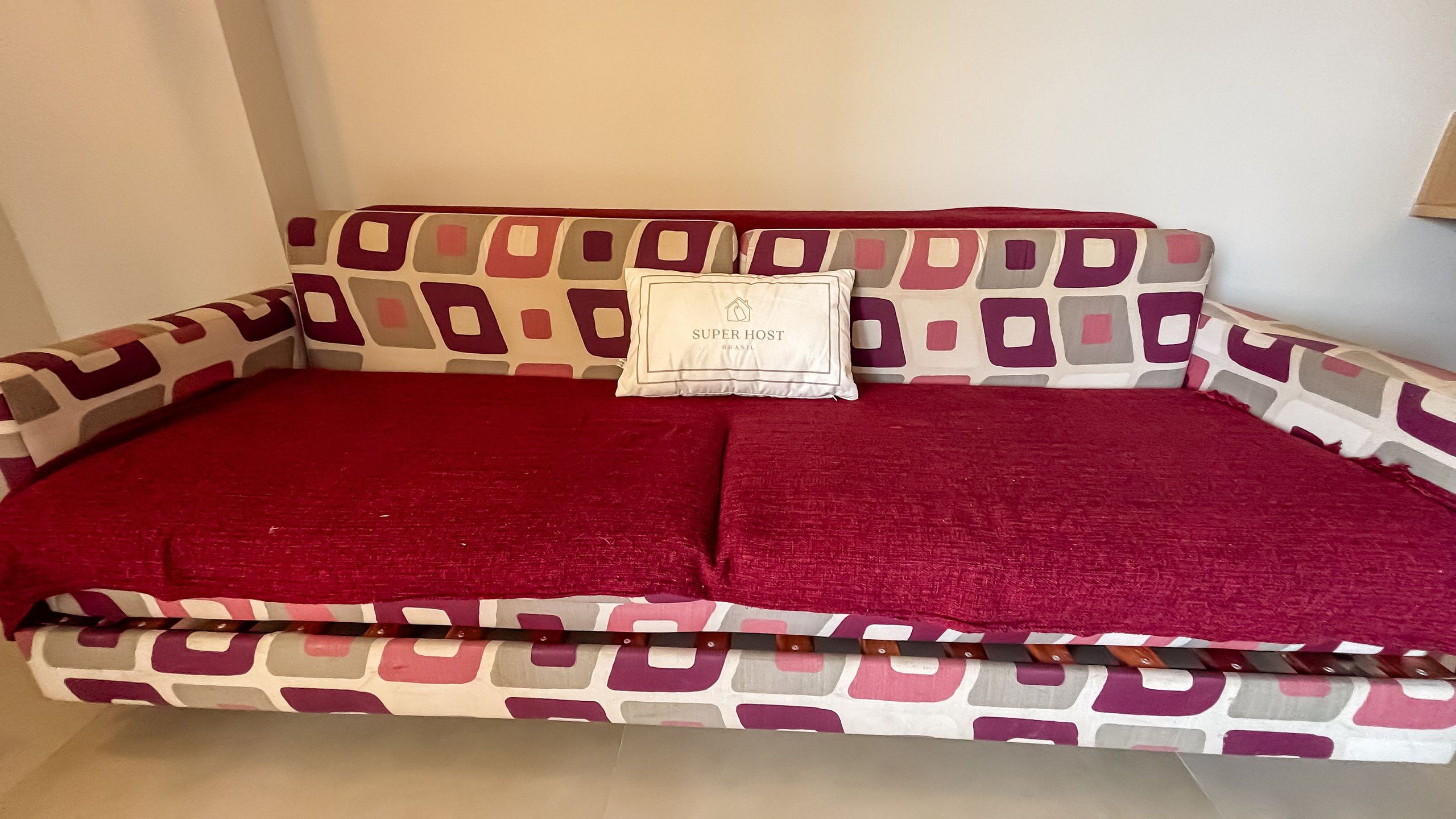 Un sofá con estampado geométrico, una manta roja y una almohada con el texto 'SUPER HOST'.