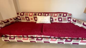 Un sofá con estampado geométrico, una manta roja y una almohada con el texto 'SUPER HOST'.