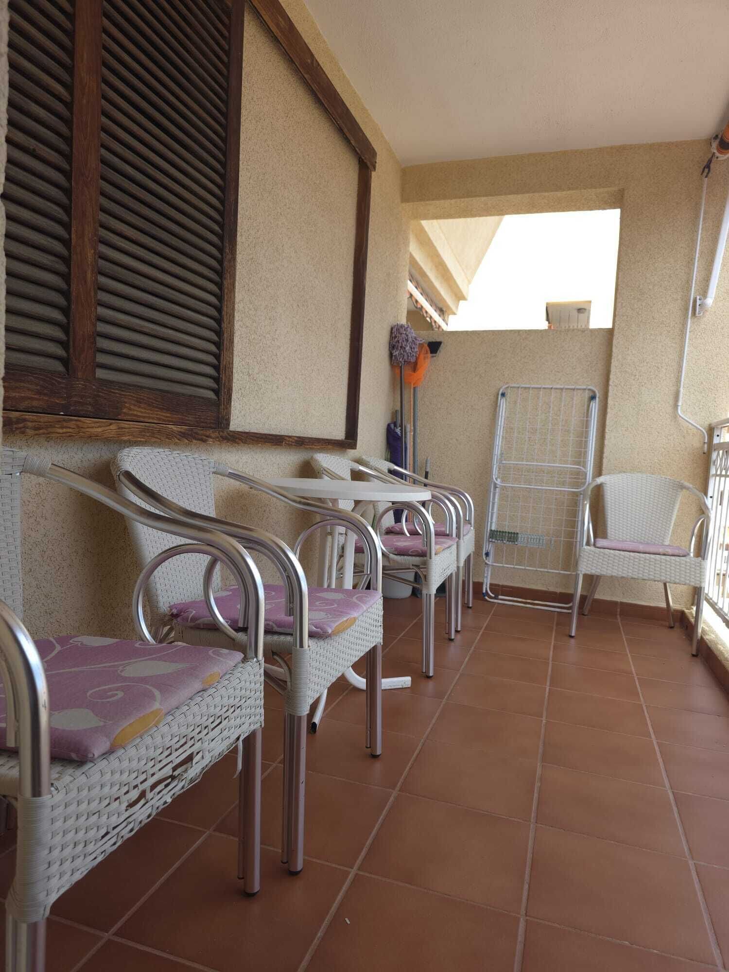 A balcony with wicker chairs, a metal chair, and a metal table.