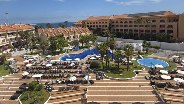 A resort with multiple swimming pools, sun loungers, and a large building with a tiled roof.
