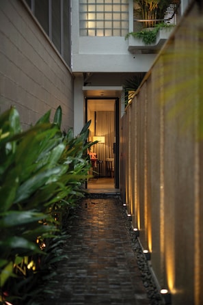 Un estrecho sendero de ladrillo que conduce a una habitación con una puerta, rodeada de paredes con iluminación vertical.