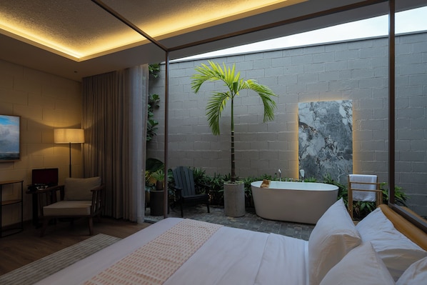 Una habitación de hotel moderna con una cama grande, un área de descanso con una silla, una mesita y una bañera.