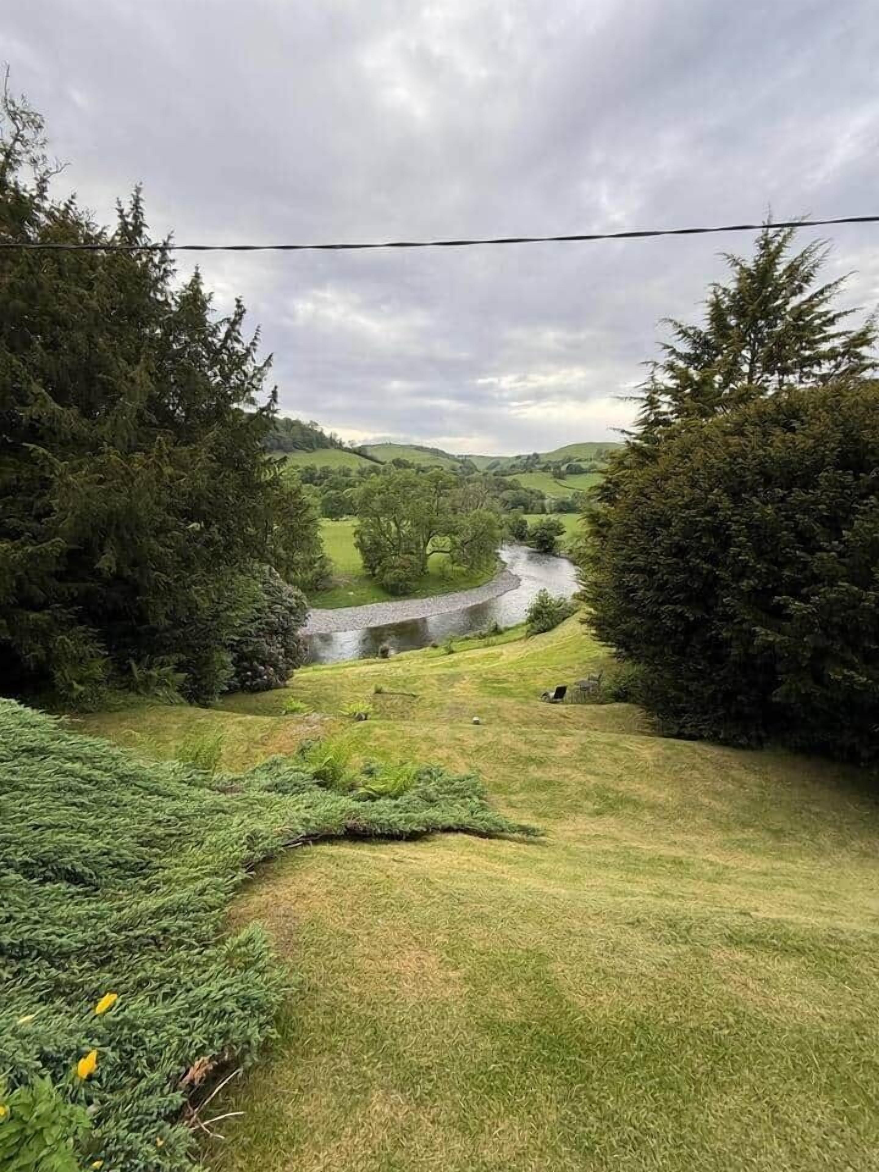 A rural landscape with a river, dense trees, and a grassy field.
