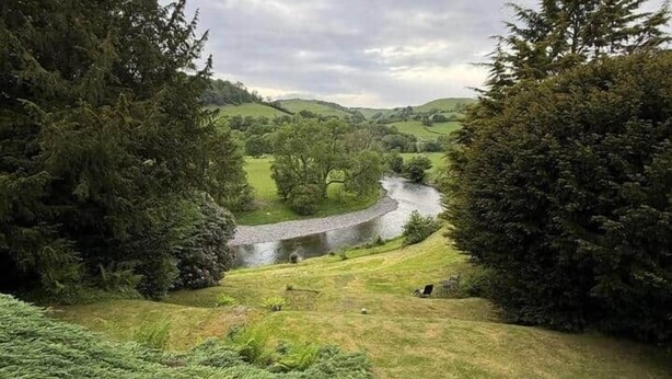 Un paisaje rural con un río, árboles densos y un campo cubierto de hierba.