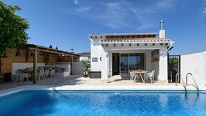 A poolside area with a covered seating area, a pool, and a building with a tiled roof. - Boho Villa Montsalvat (Pego)
