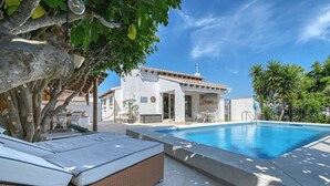 Zona de piscina amb una cadira relaxant, un edifici amb teulada d'aquarella i un cel blau radiant.