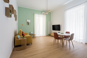 Un salon moderne comprenant un canapé, une table à manger avec des chaises, un téléviseur à écran plat et une grande fenêtre avec des rideaux.