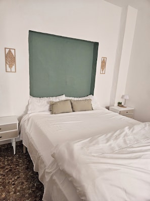 A neatly made bed with a white comforter and two pillows, a white nightstand with a drawer, and a wall with two decorative leaf motifs. - Perfect for relaxing and close to everything! Perfect if you're looking for peace and quiet and convenience (Antequera)