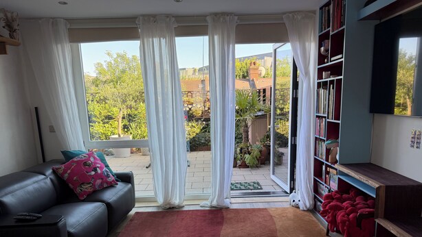A living room with a black leather sofa, a red rug, a bookshelf, and a sliding glass door leading to a patio with plants. - Lovely 3-bedroom house in tranquil London perfect for your stay -sleeps 6 (London)