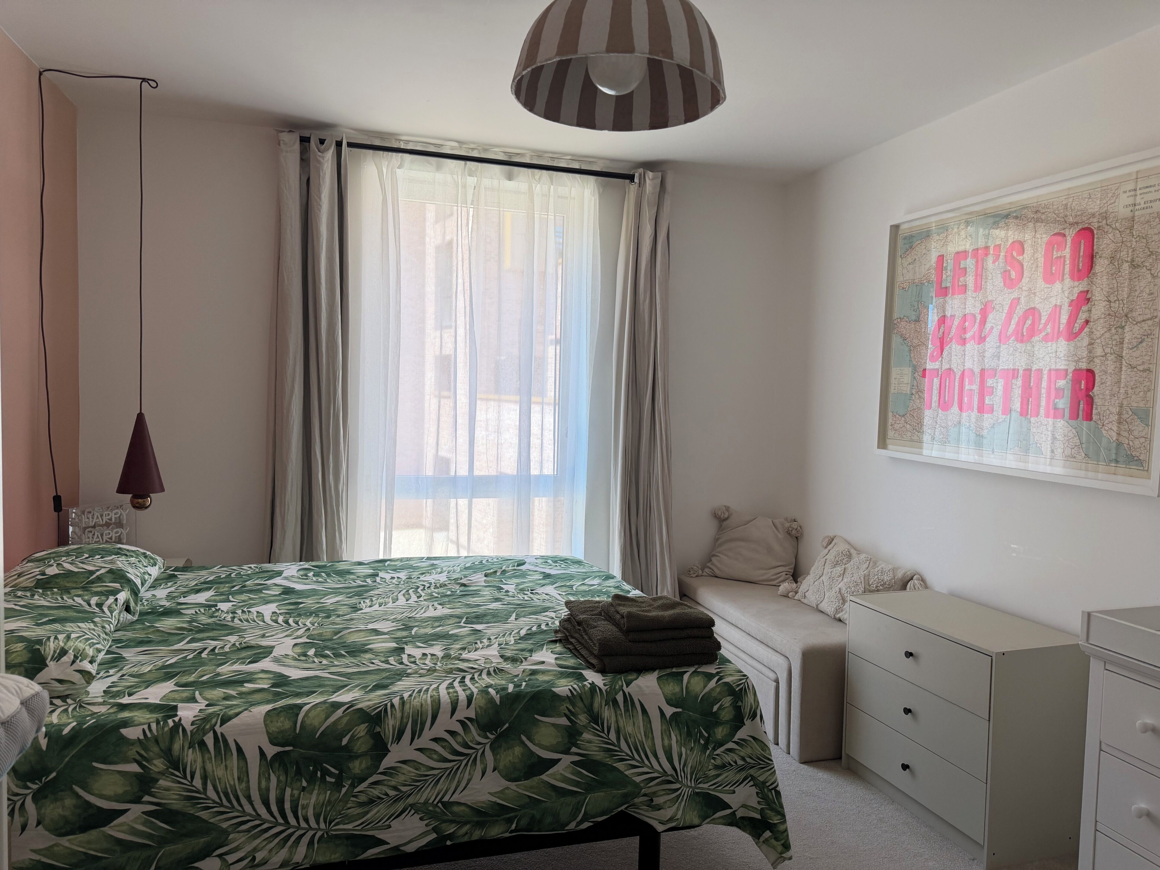 Une chambre à coucher avec un lit, une fenêtre avec des rideaux, une carte accrochée au mur et une table de chevet.