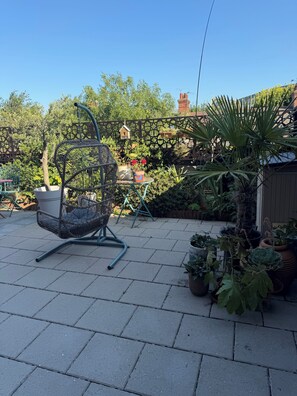 A patio with a wicker chair, potted plants, and a wooden fence.