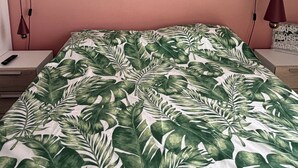 A bed with a tropical leaf pattern bedspread, a bedside table with a remote control, and a wall-mounted lamp. - Lovely 3-bedroom house in tranquil London perfect for your stay -sleeps 6 (London)