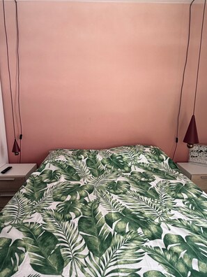 A bed with a tropical leaf pattern bedspread, a bedside table with a remote control, and a wall-mounted lamp.