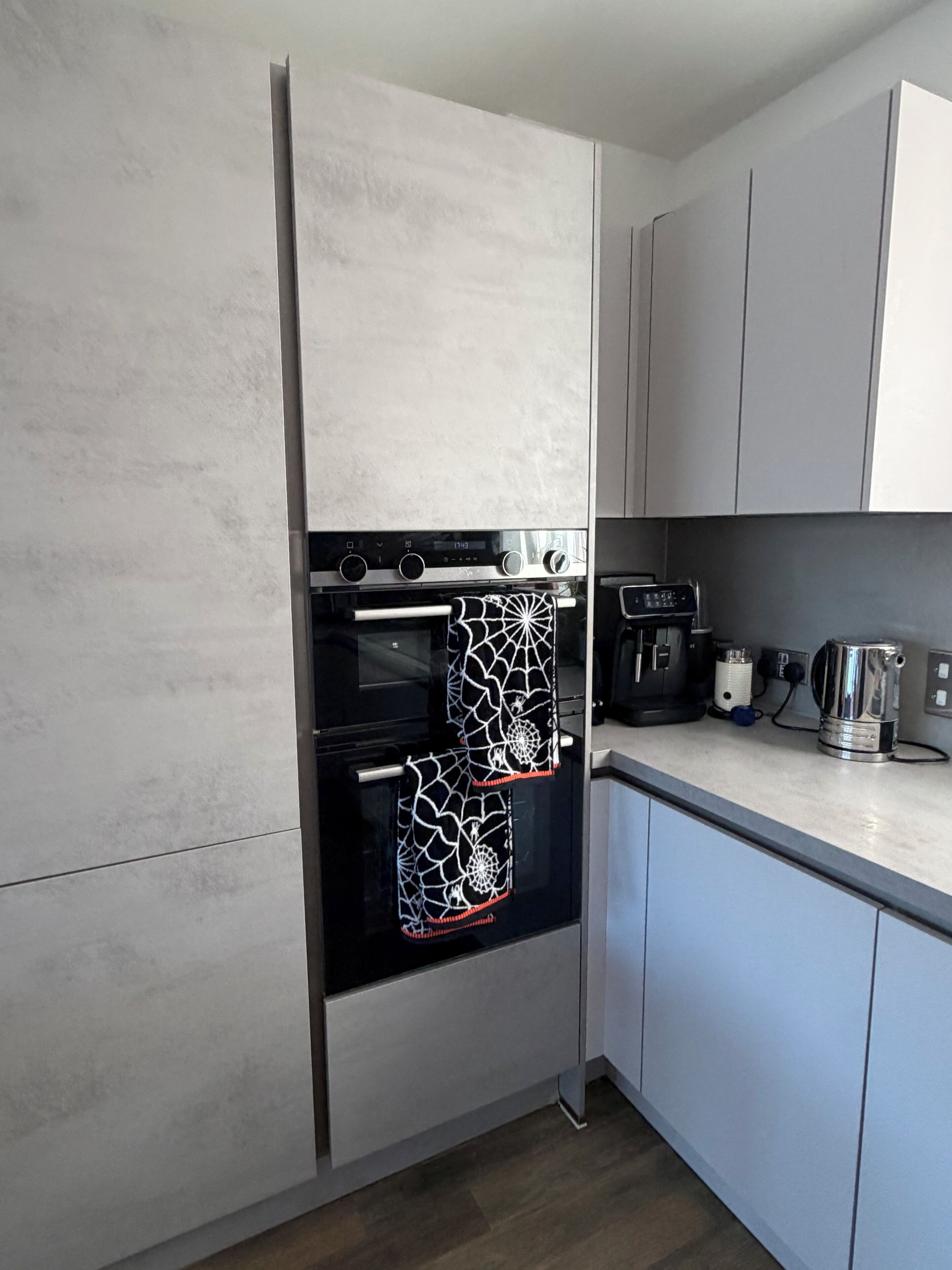 A kitchen with a built-in oven, a coffee maker, and a kettle on the countertop.
