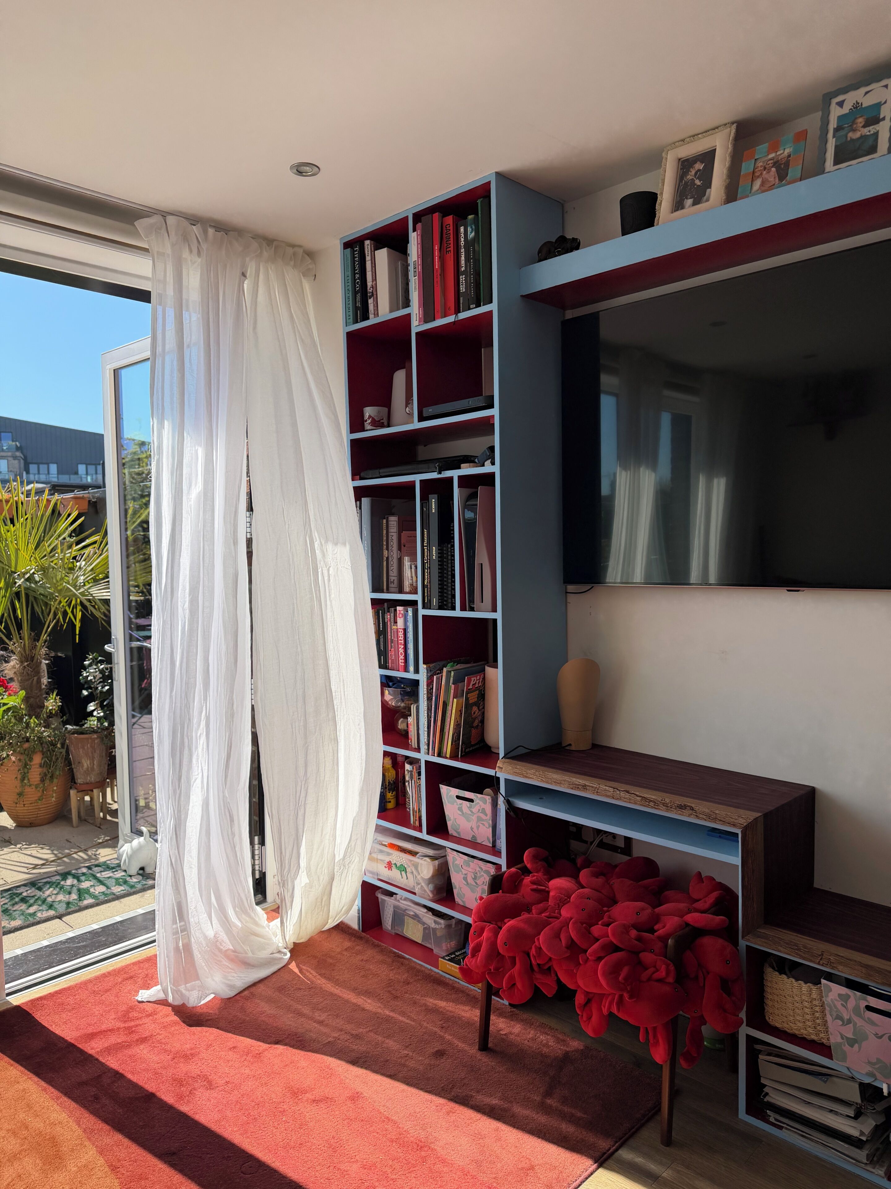 A room with a bookshelf, a TV, a red sofa, and a window with curtains.