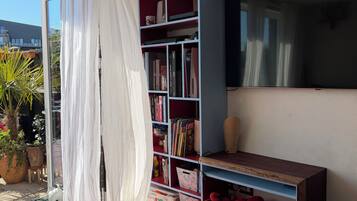 A room with a bookshelf, a TV, a red sofa, and a window with curtains.