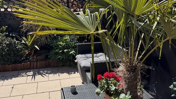 A patio with a wicker sofa, potted plants, and a stone wall in the background.