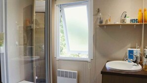 A bathroom with a shower, a window, a sink, and a shelf with toiletries. - Cottage in a Natural Domain P10 (Saint-Privat-de-Champclos)