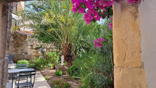 A stone archway with vibrant purple bougainvillea flowers, a stone pathway, and a seating area with chairs. - The scent of calicanto (Tresnuraghes)
