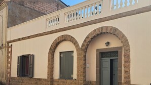 A building with a beige facade, stone arches, and a balcony with decorative railings. - The scent of calicanto (Tresnuraghes)